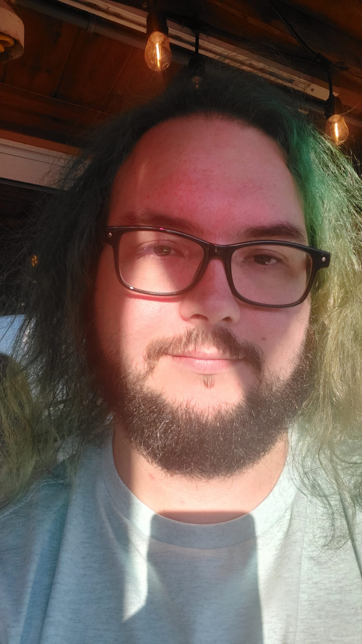 A man with green hair is sitting on a patio in the sunlight, Photo 5